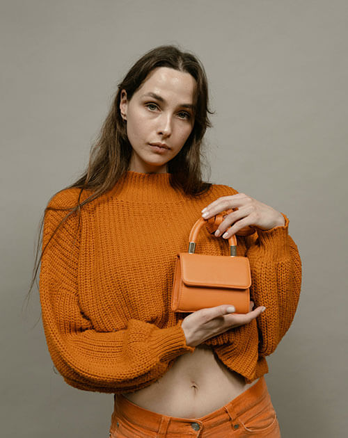 A woman in an orange dress is holding a bag.